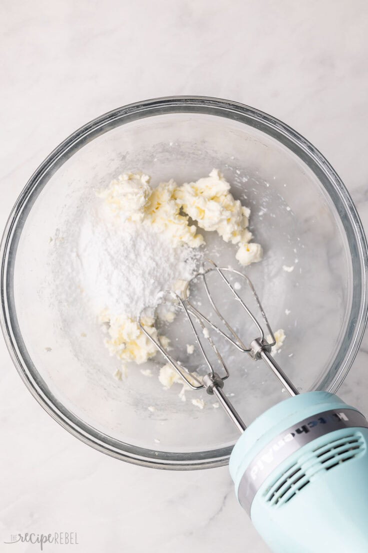 cream cheese and powdered sugar in glass mixing bowl with mixer beside.