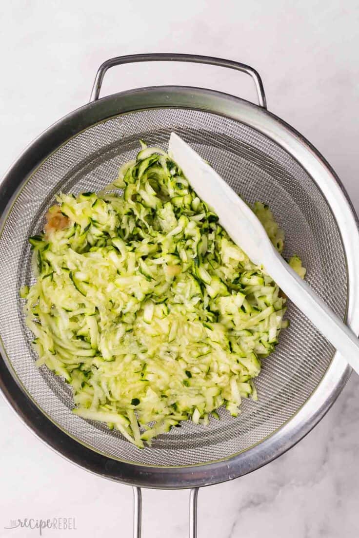 shredded apple and zucchini in a steel strainer.
