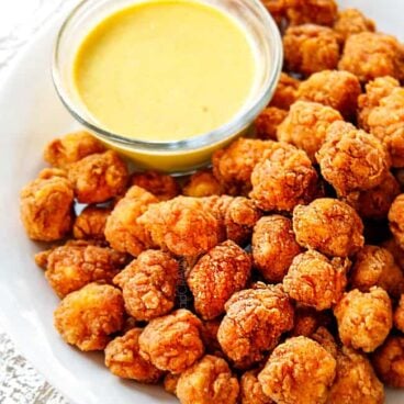 popcorn chicken on a white plate with a side of honey mustard