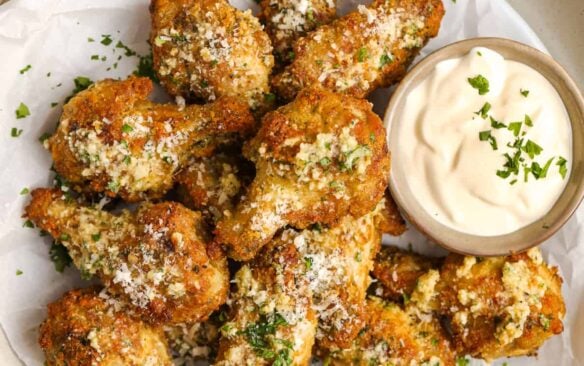 garlic parmesan wings on a white plate with a side of sauce