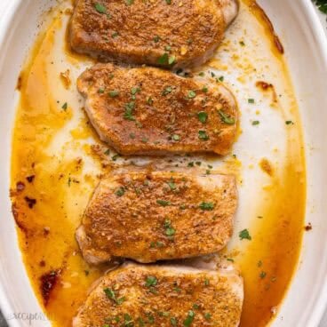 baked pork chops in baking dish topped with chopped parsley.