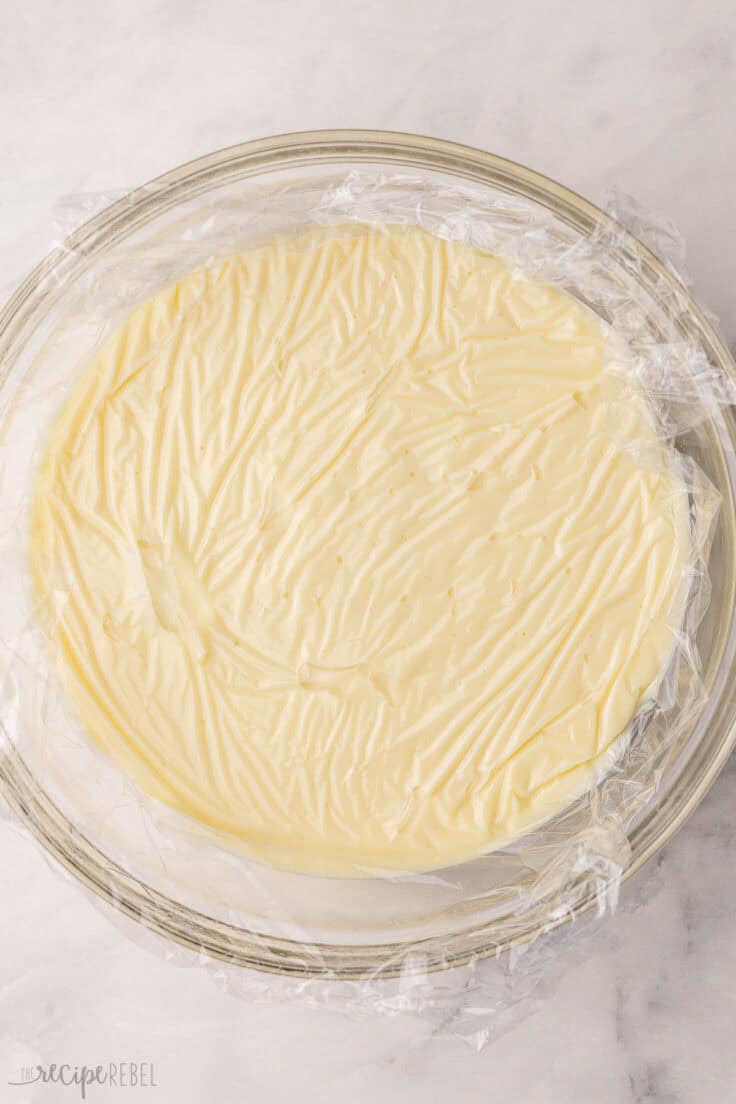 glass mixing bowl full of pudding with plastic wrap over the top.