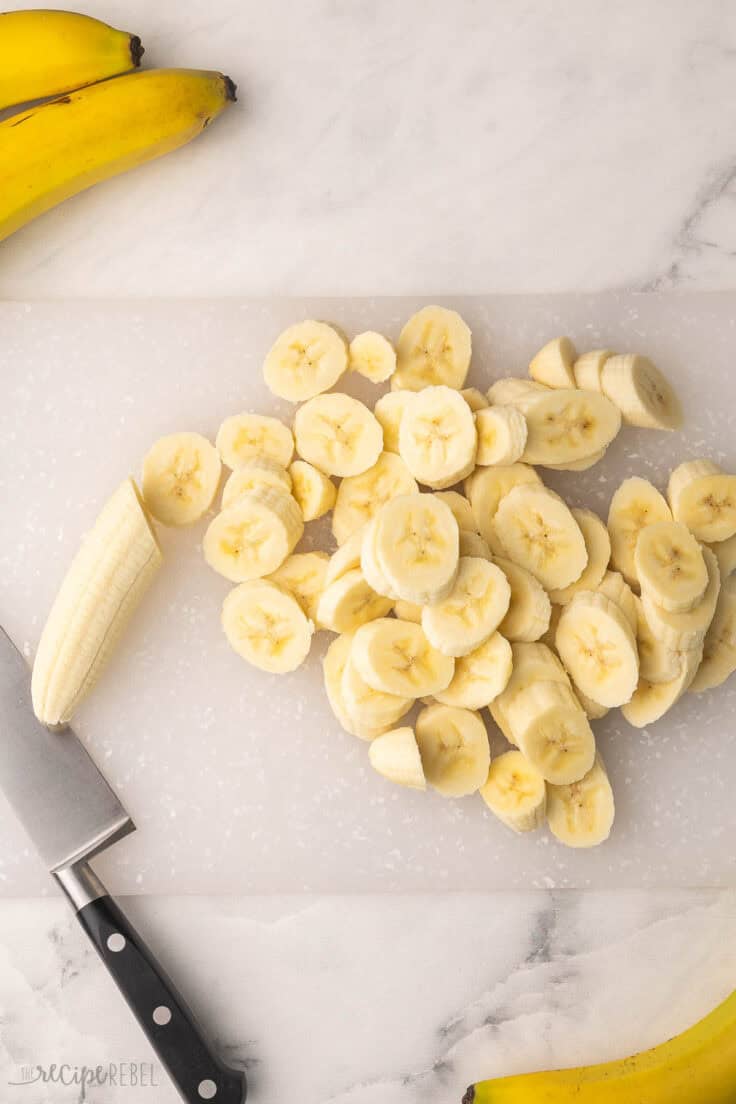 sliced bananas on a cutting board with knife beside.