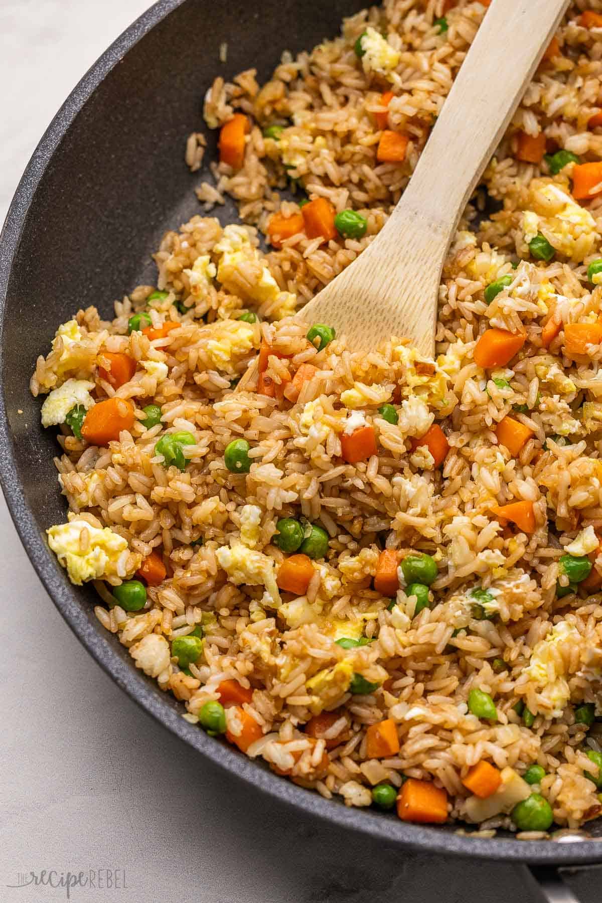 a wooden ladle scooping fried rice out of pan.