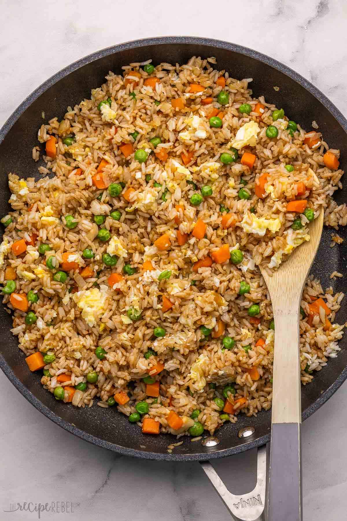 Skip the takeout and make this simple Fried Rice at home! With soy sauce, toasted rice, vegetables and eggs, it's delicious on its own or paired with your favorite main dish. #rice #dinner #recipe | easy dinner ideas | asian food | chinese food | rice recipes | easy fried rice | frozen vegetables black pan full of fried rice with wooden ladle.