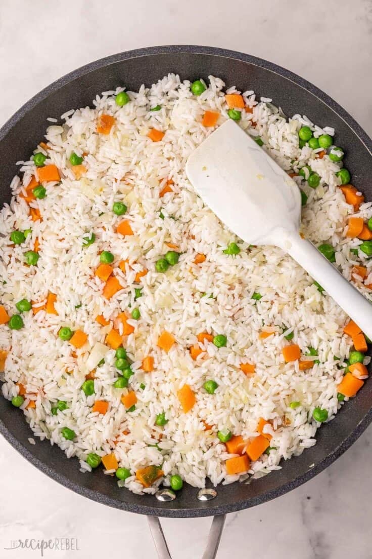 rice added to other ingredients in black pan.