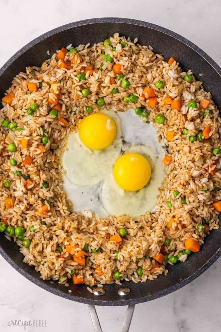 two eggs being fried in the center of pan with fried rice beside.
