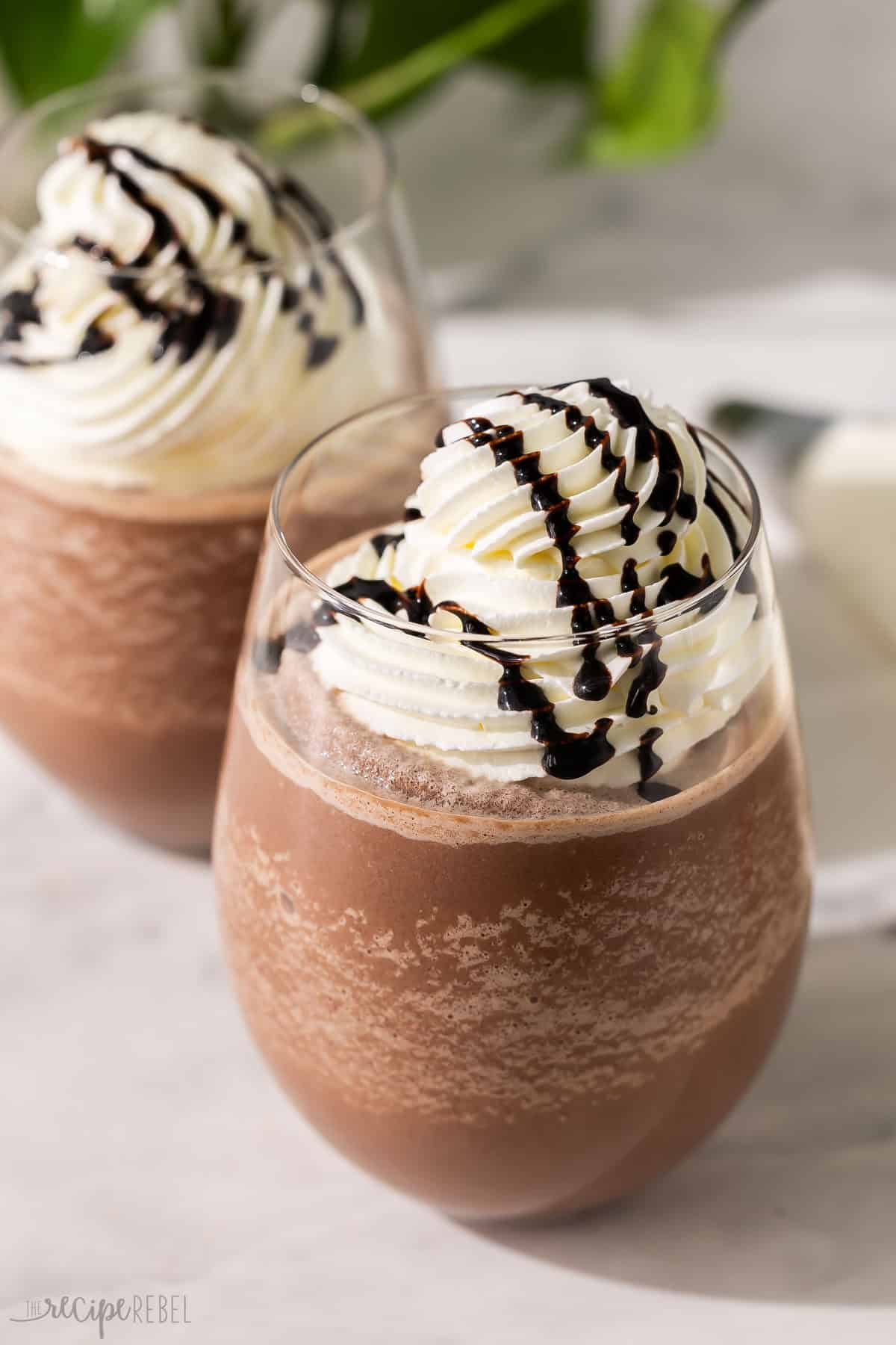 This Frozen Hot Chocolate is made with hot chocolate mix, hot fudge sauce, milk, and ice for a creamy treat with loads of refreshing, chocolatey flavor! Super customizable and perfect for hot summer days. #drink #chocolate | summer drinks | drink recipe | chocolate drink | chocolate milkshake | summer treat two glasses of frozen hot chocolate topped with chocolate sauce.