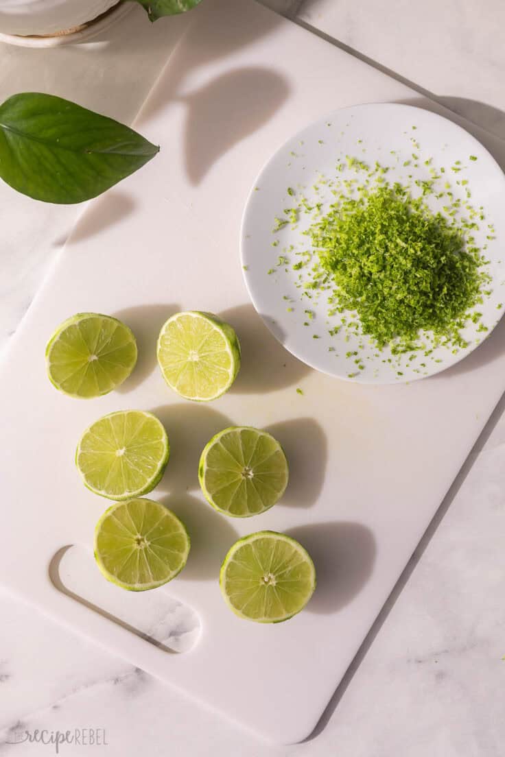 halved limes on a cutting board with a plate of lime zest beside.