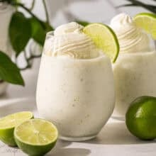 two glasses of frozen limeade topped with whipped cream.
