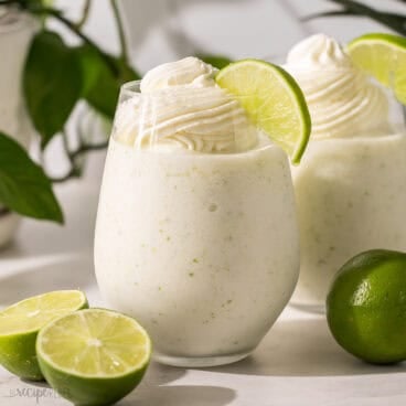two glasses of frozen limeade topped with whipped cream.
