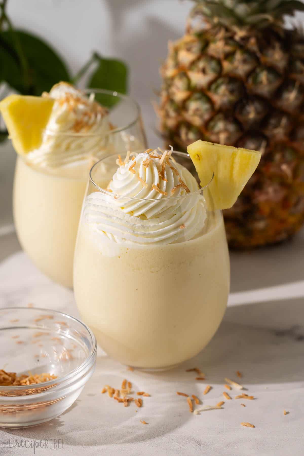 two glasses of pina colada slushy topped with whipped cream.
