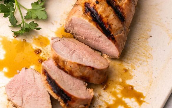 slices of pork tenderloin on a cutting board with parsley behind it.