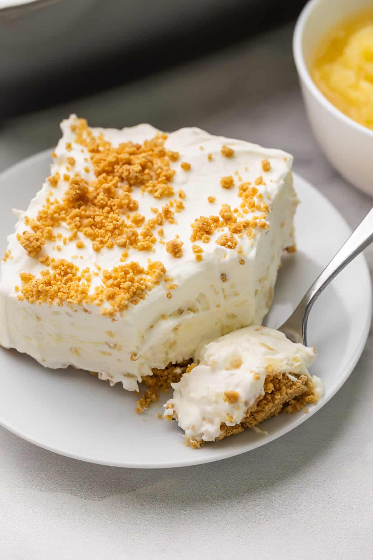 This no bake Pineapple Dessert has loads of crushed pineapple, a no bake graham cracker crust, and a cream cheese filling. Perfect for spring or Easter! #pineapple #dessert #recipe | no bake dessert | no bake recipes | cream cheese dessert | no bake cheesecake | easter dessert | spring recipe | summer desserts a fork full of pineapple dessert being scooped off plate.