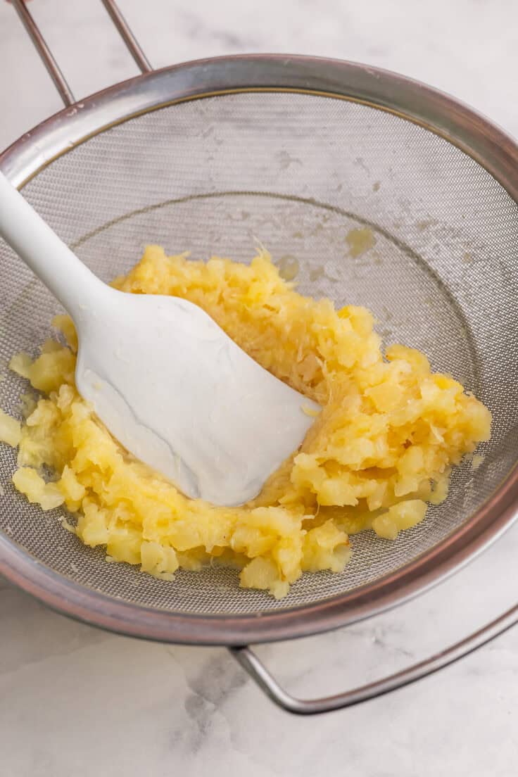 pineapple juice being squeezed out in strainer by white spatula.