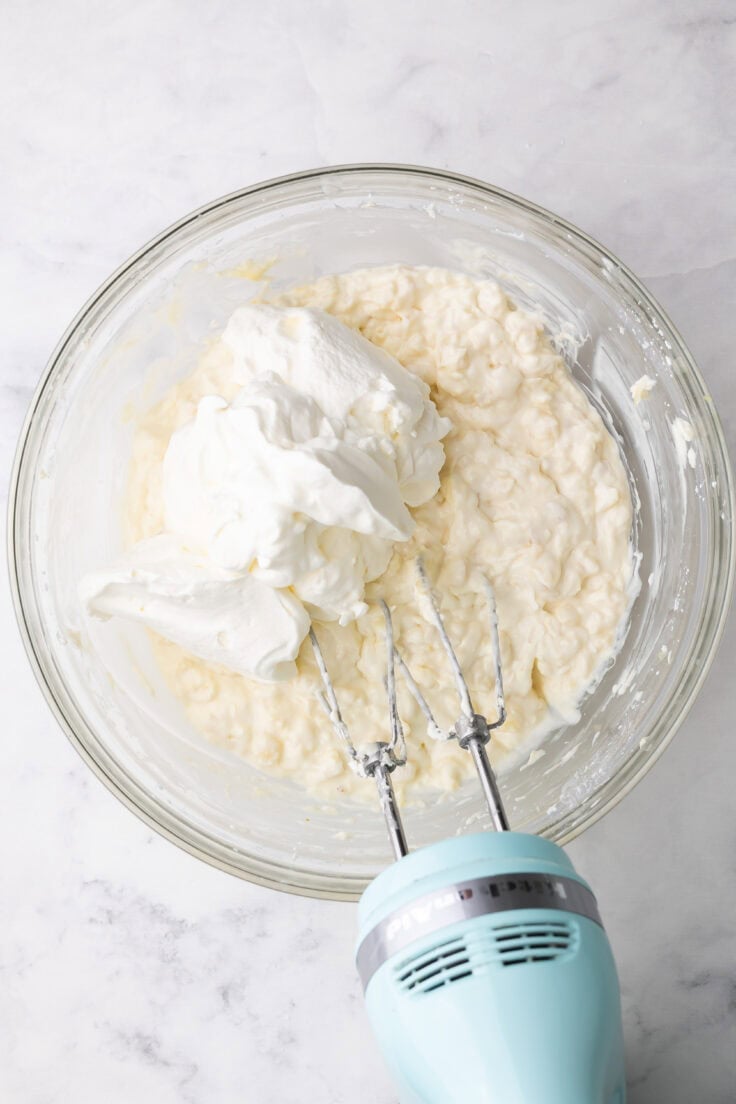 whipped cream added to other ingredients in glass mixing bowl.
