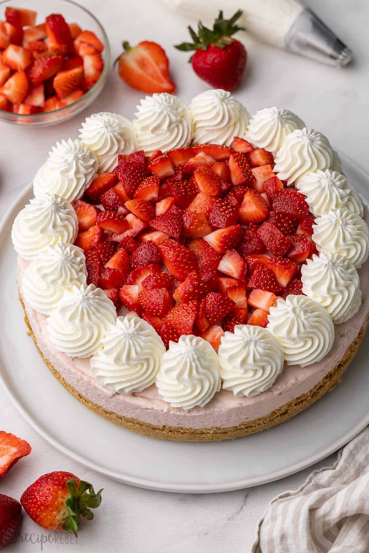 This No Bake Strawberry Cheesecake is a dreamy dessert with a graham cracker crust and a velvety cream cheese filling made with fresh strawberry sauce! Just 30 minutes to prep before chilling overnight for the perfect sliceable texture. #cheesecake #strawberry #dessert | no bake dessert | no bake cheesecake | cream cheese dessert | strawberry dessert | summer dessert recipe strawberry cheesecake on a white plate with strawberries beside.