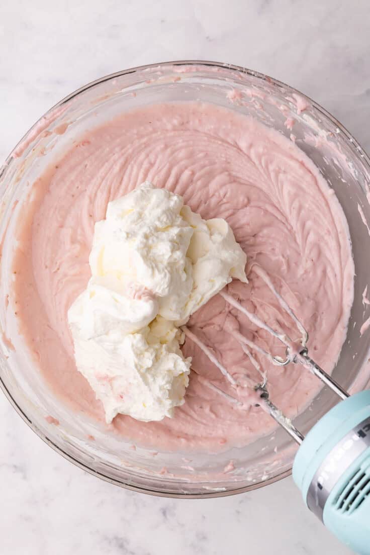 whipped cream added to top of mixed ingredients in glass bowl.