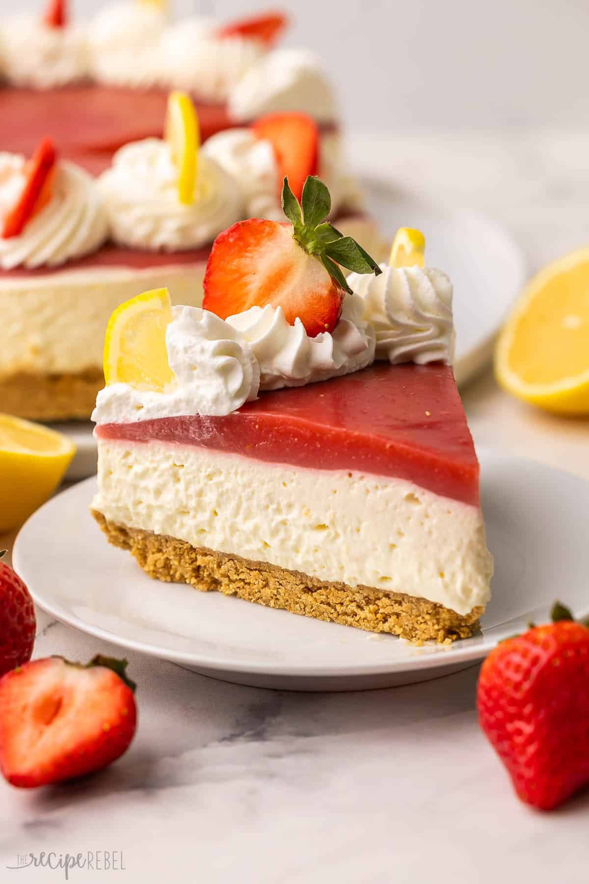 The No Bake Strawberry Lemonade Cheesecake is made with a lemon cheesecake filling and homemade graham cracker crust, and topped with strawberry sauce for a sweet and tangy treat! Prepped in 25 minutes and can be made ahead of time. #nobake #cheesecake #dessert | no bake dessert | dessert recipes | easy desserts | lemon desserts | strawberry recipes | cheesecake recipe | summer dessert strawberry lemonade cheesecake on a white plate with strawberries and lemons beside.