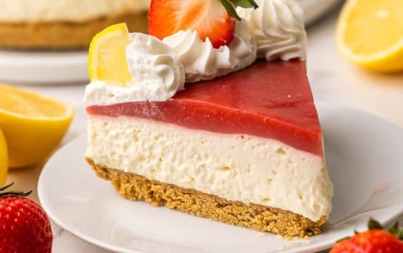 a piece of strawberry lemonade cheesecake on a white plate with the cake in the background.