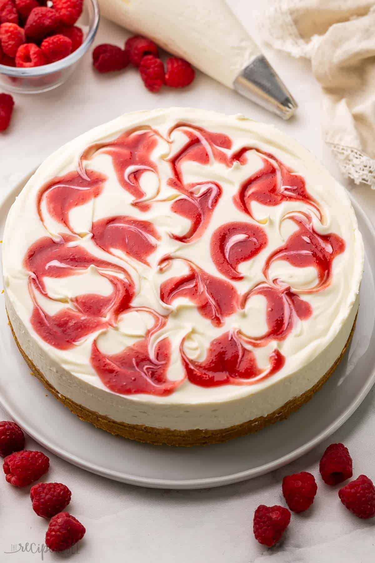 white chocolate raspberry cheesecake on a large white plate with raspberries around it.
