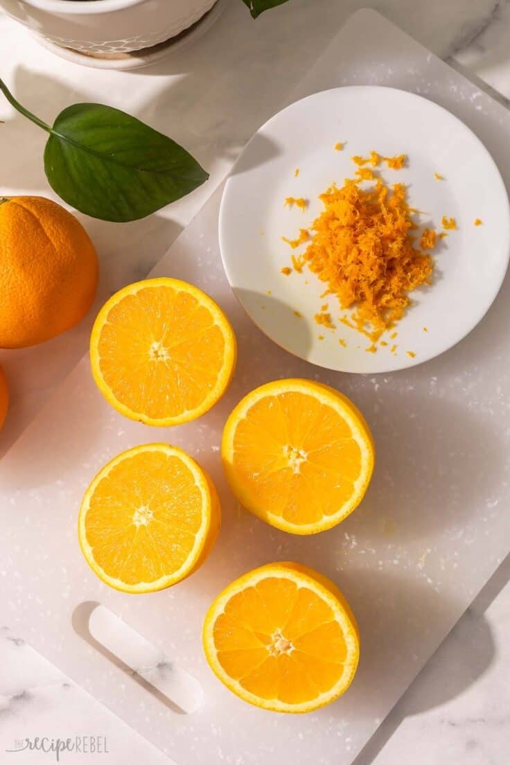 sliced oranges on a cutting board with a plate of orange zest beside.