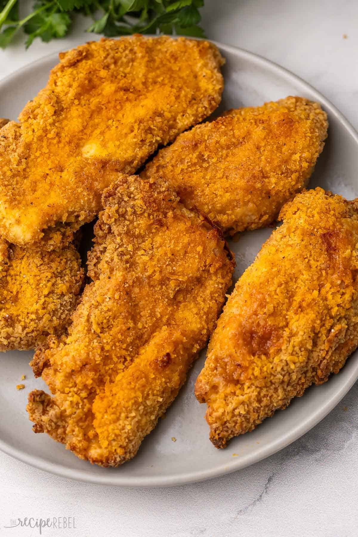 a plate filled with oven fried chicken with parsley behind.