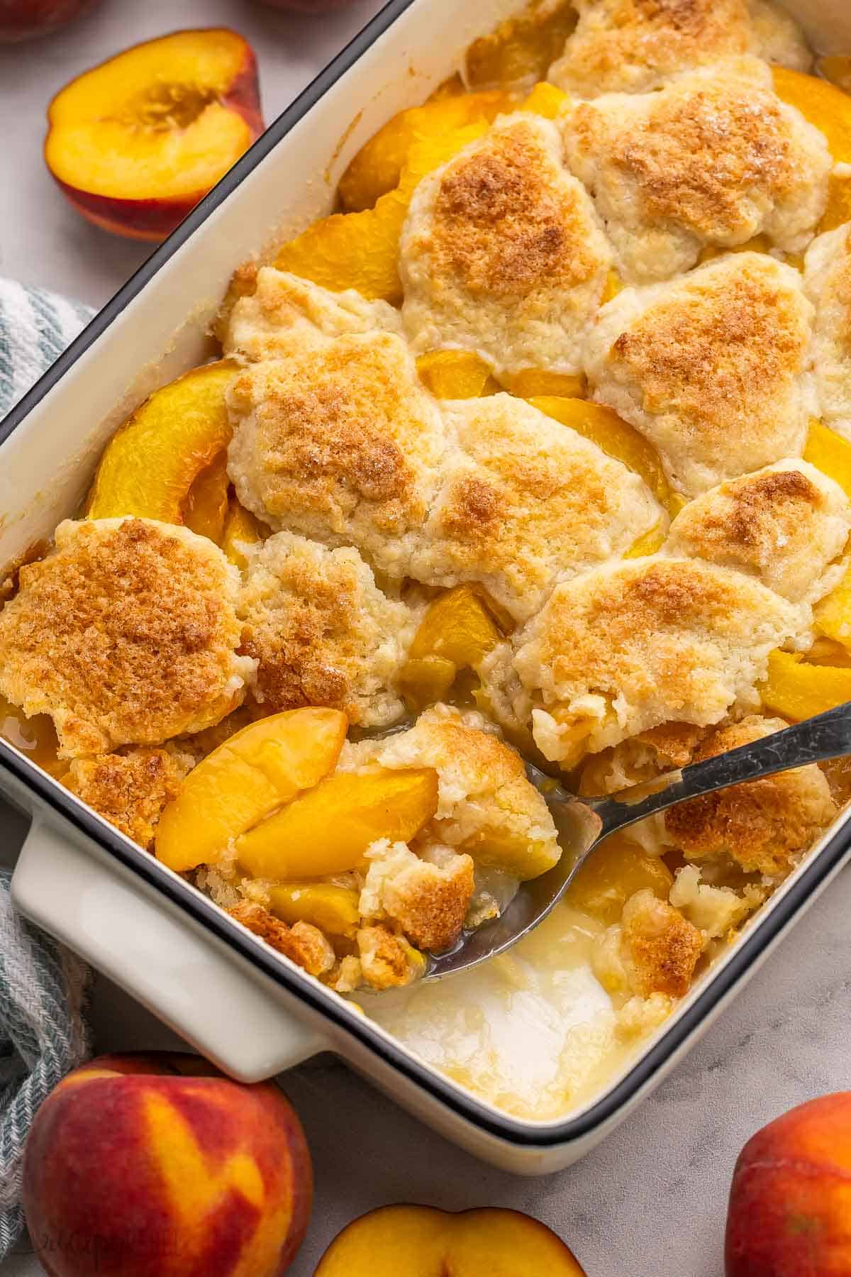 a spoon scooping peach cobbler out of pan.