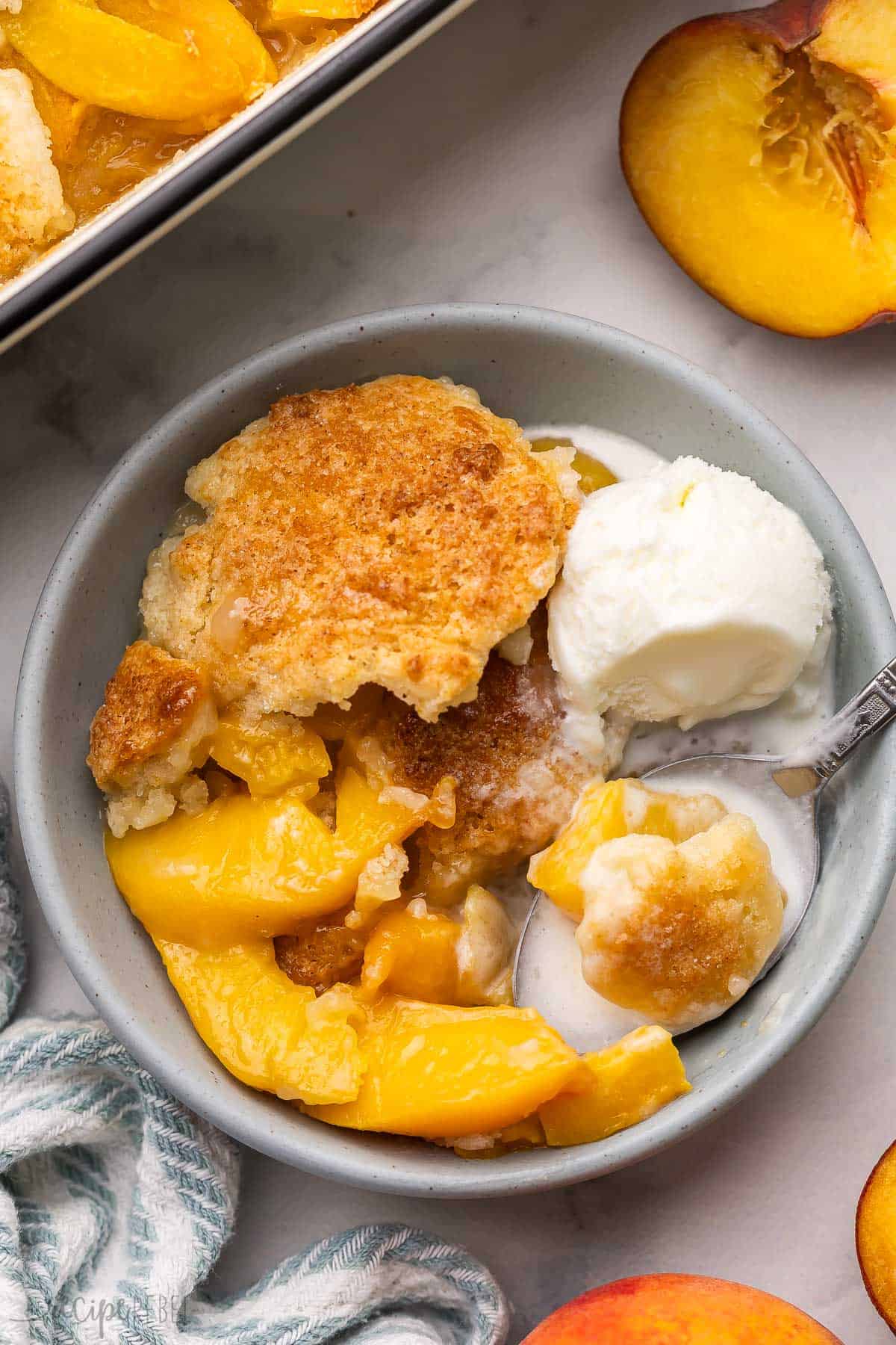 a bowl of peach cobbler with ice cream and a spoon.