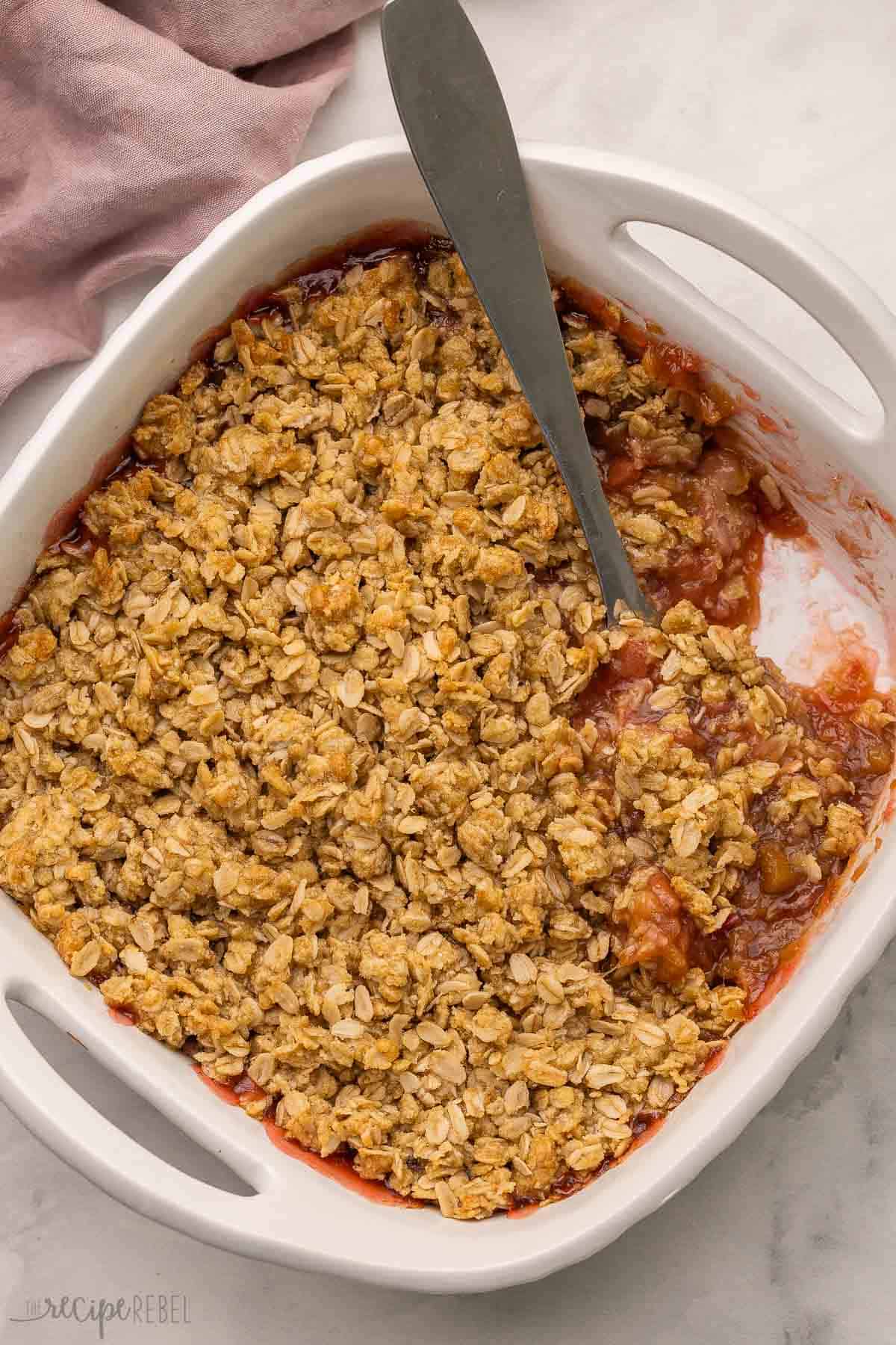 This Rhubarb Crisp recipe is packed with a tangy rhubarb filling and topped with a crunchy oatmeal streusel! Add a big scoop of vanilla ice cream on top for a sweet and tart dessert that's ready in 45 minutes. #rhubarb #dessert #recipe | dessert recipes | rhubarb recipes | rhubarb dessert | fruit crisp | baking recipe | easy recipes a ladle in a pan of rhubarb crisp.