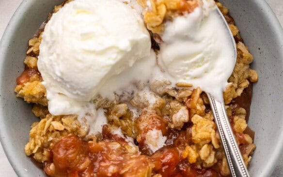 rhubarb crisp in a bowl topped with a scoop of vanilla ice cream.