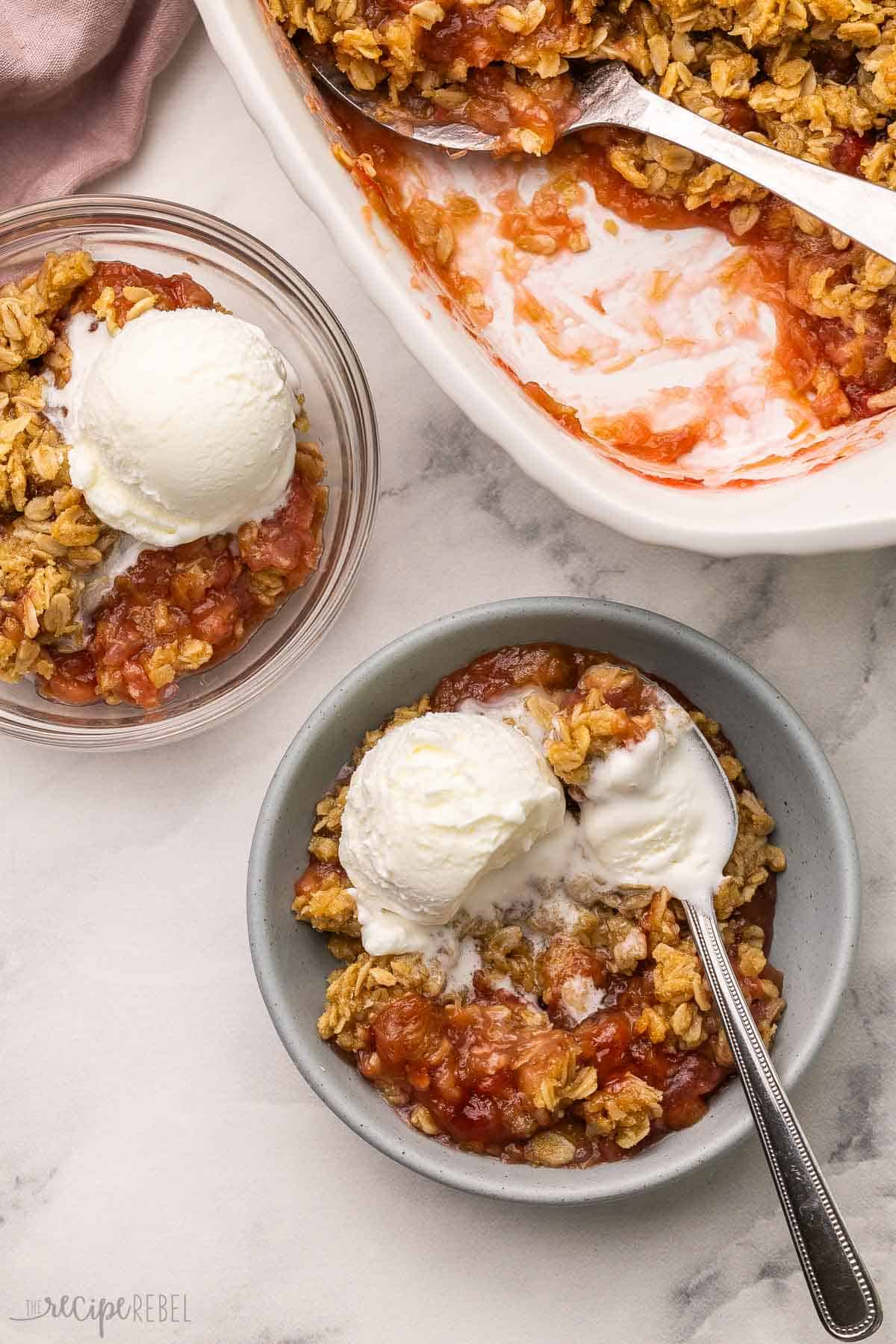 This Rhubarb Crisp recipe is packed with a tangy rhubarb filling and topped with a crunchy oatmeal streusel! Add a big scoop of vanilla ice cream on top for a sweet and tart dessert that's ready in 45 minutes. #rhubarb #dessert #recipe | dessert recipes | rhubarb recipes | rhubarb dessert | fruit crisp | baking recipe | easy recipes bowls of rhubarb crisp with a spoon and vanilla ice cream.