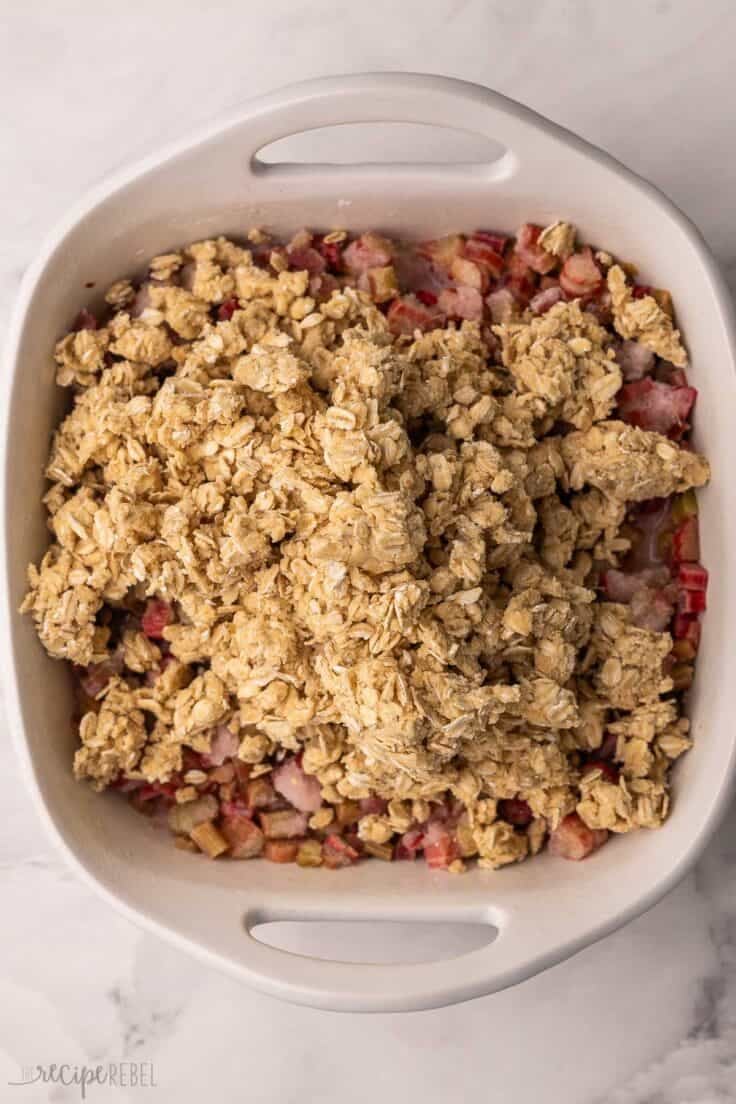white baking dish with topping added to rhubarb.