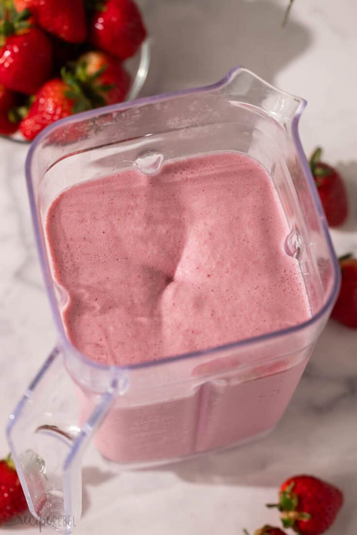 a full blender of strawberry frappuccino with strawberries around it.