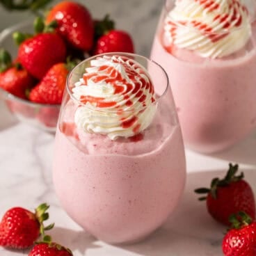 strawberry frappuccinos in glasses with strawberries beside.