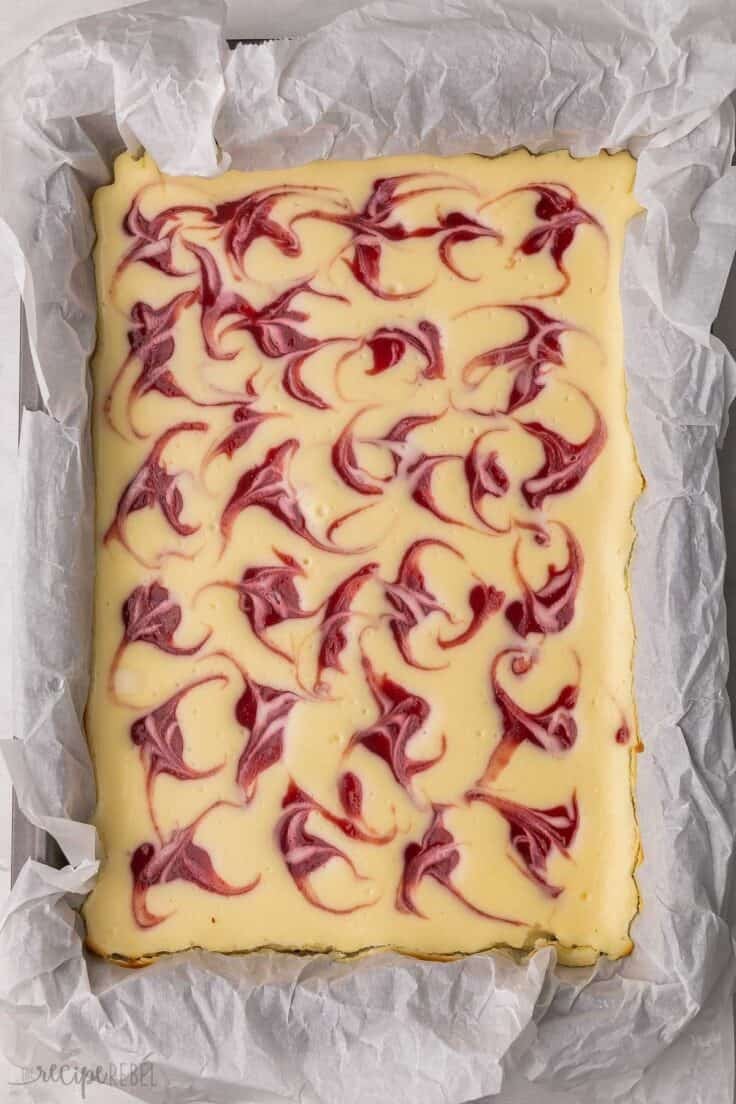 strawberry swirl cheesecake in pan lined with parchment.