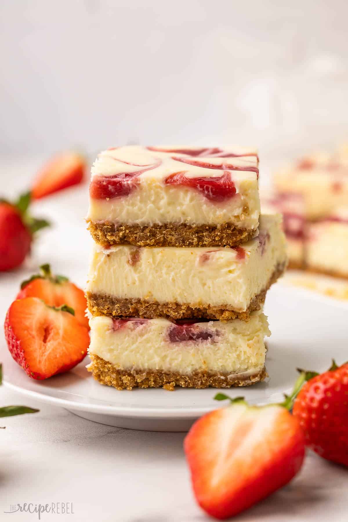three stacked up strawberry swirl cheesecake bars on a white plate.