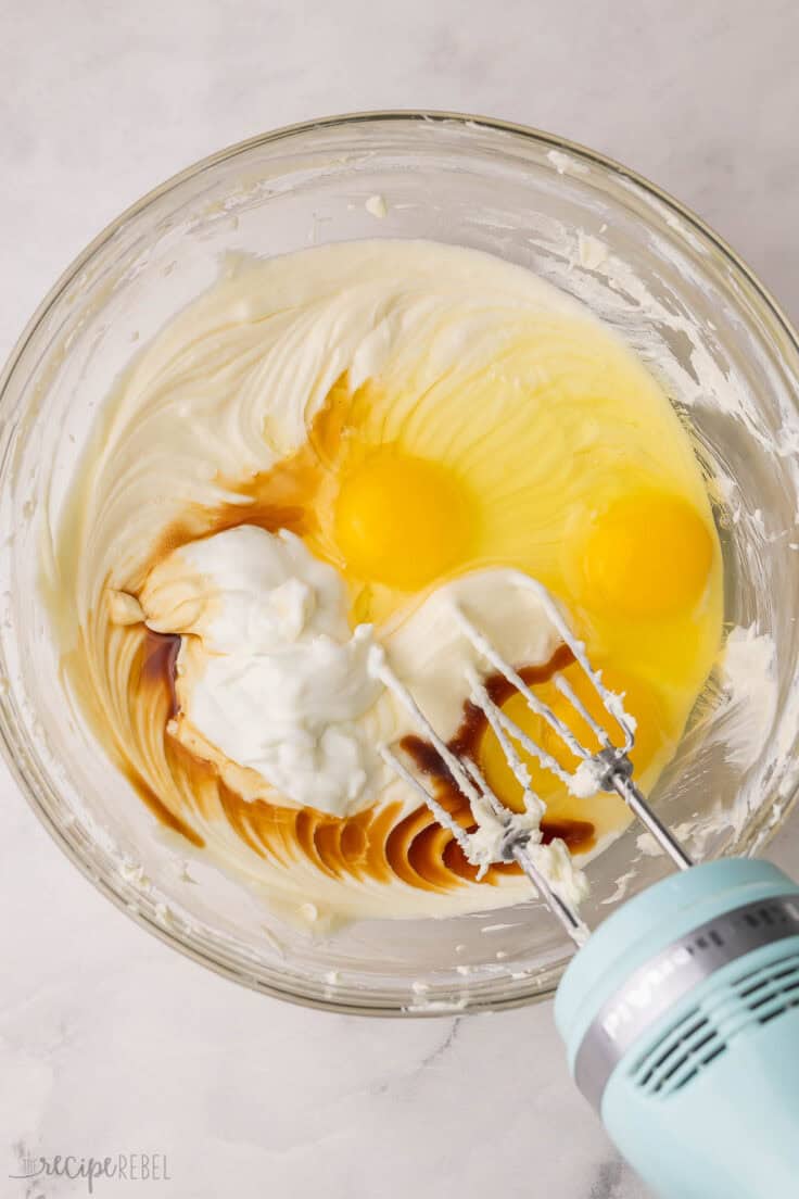eggs added to other ingredients in glass bowl with mixer beside.