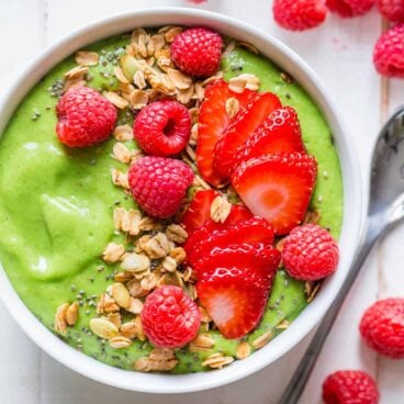green smoothie bowl topped with fresh fruit and granola.