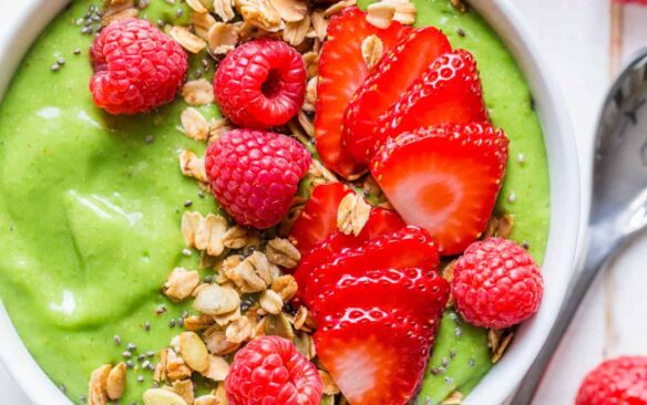 green smoothie bowl topped with fresh fruit and granola.