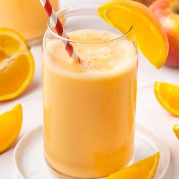 orange smoothie in a glass with a straw and orange wedge.