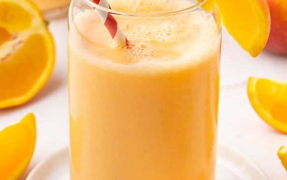 orange smoothie in a glass with a straw and orange wedge.