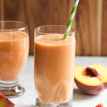 peach carrot smoothie in a glass with a green and white straw.