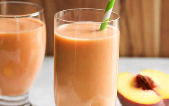 peach carrot smoothie in a glass with a green and white straw.