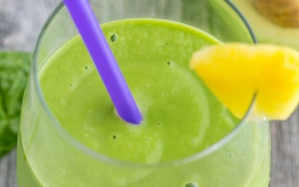 pineapple avocado smoothie in a glass with a purple straw.