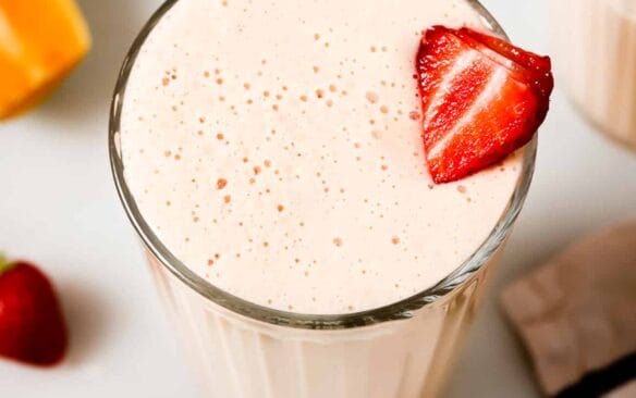 strawberry papaya smoothie in a glass garnished with a strawberry.