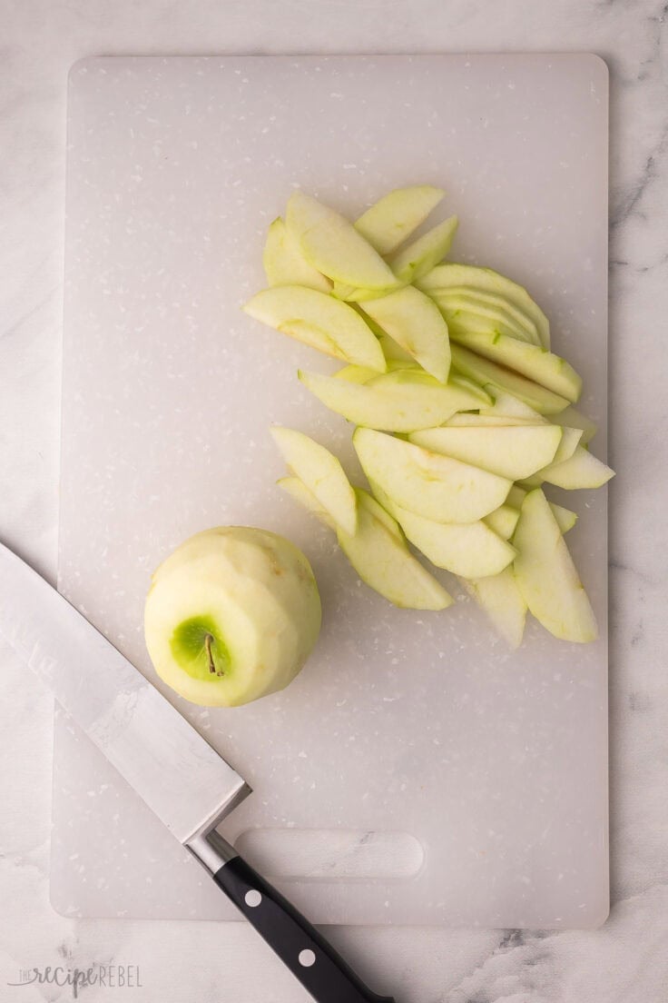 apple slices and a peeled apple on a white cutting board.