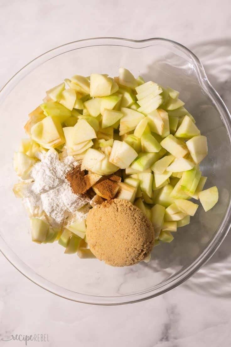 chopped apples and other ingredients in glass mixing bowl.