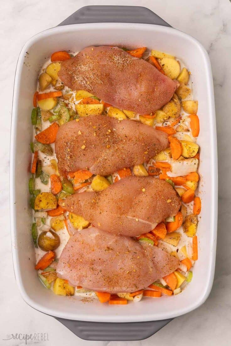 four chicken breast on top of uncooked vegetables in pan.