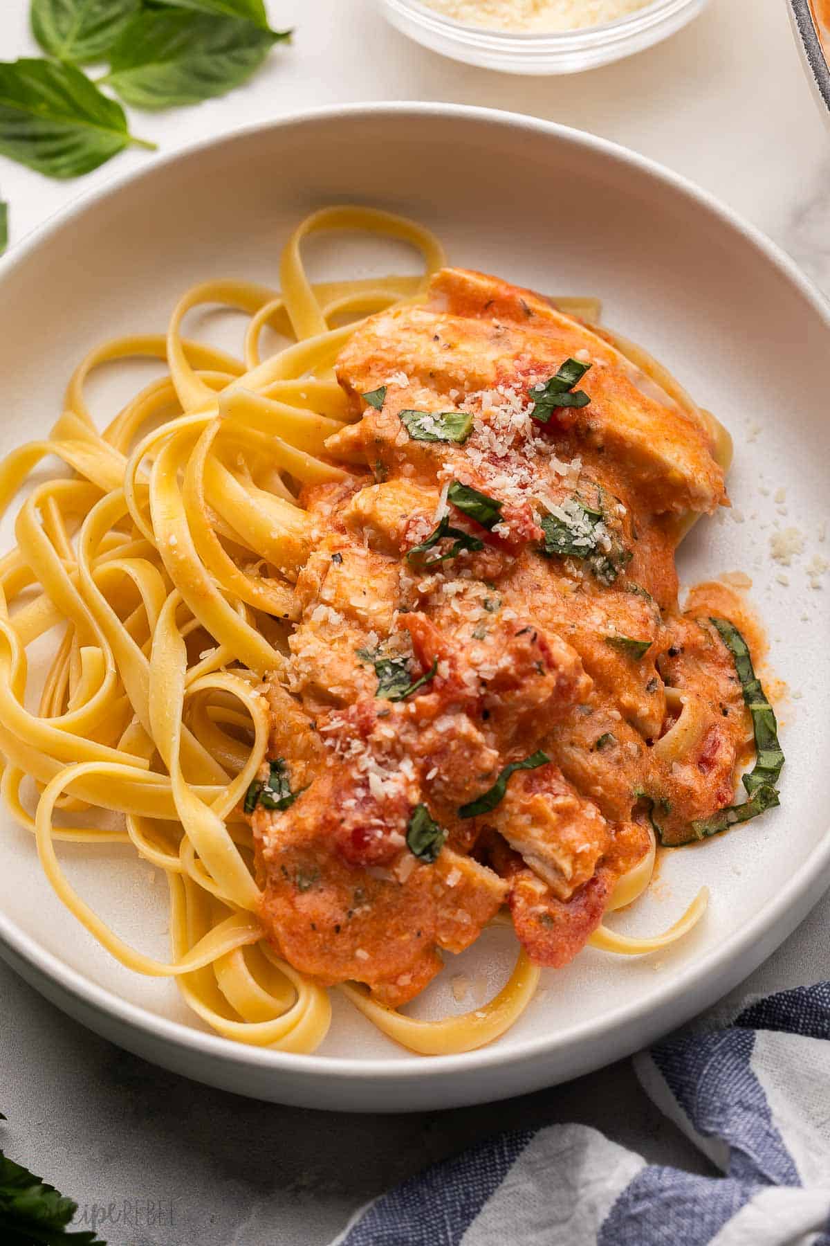 pasta on a plate topped with a tomato basil chicken breast.